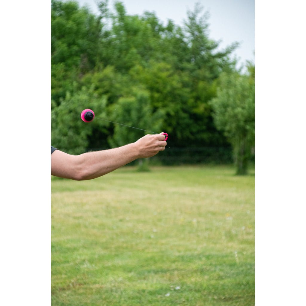 Person holding a pink and black object in an outdoor setting with greenery.