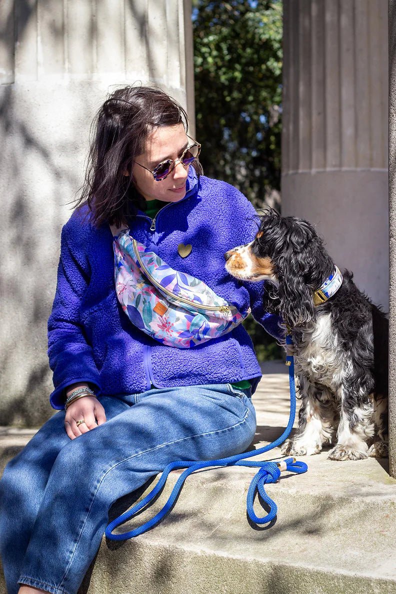 Woman in a blue sweater and jeans sitting on steps with a dog on a leash.