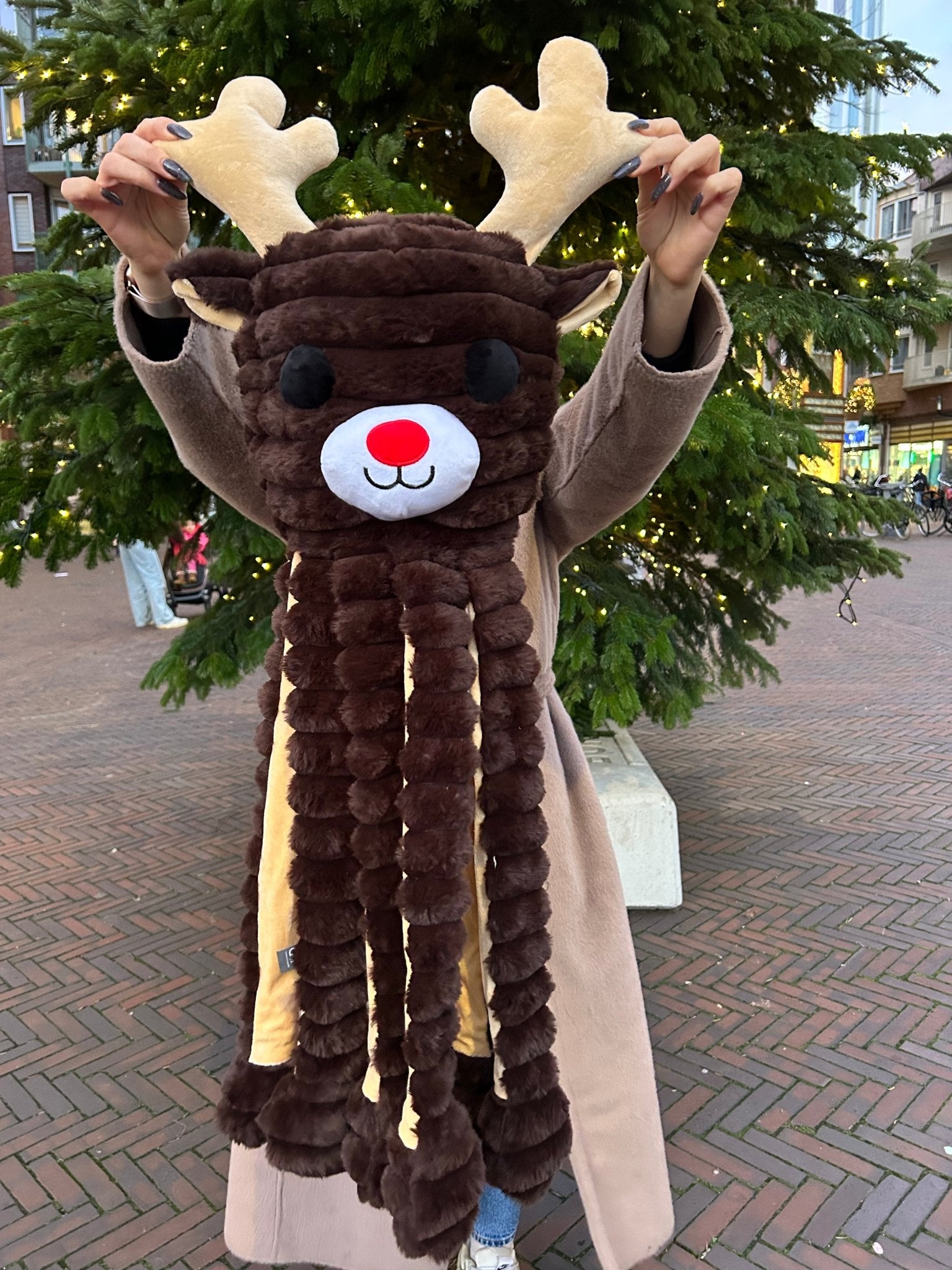 Person wearing a reindeer-themed scarf in an urban setting with trees and buildings.