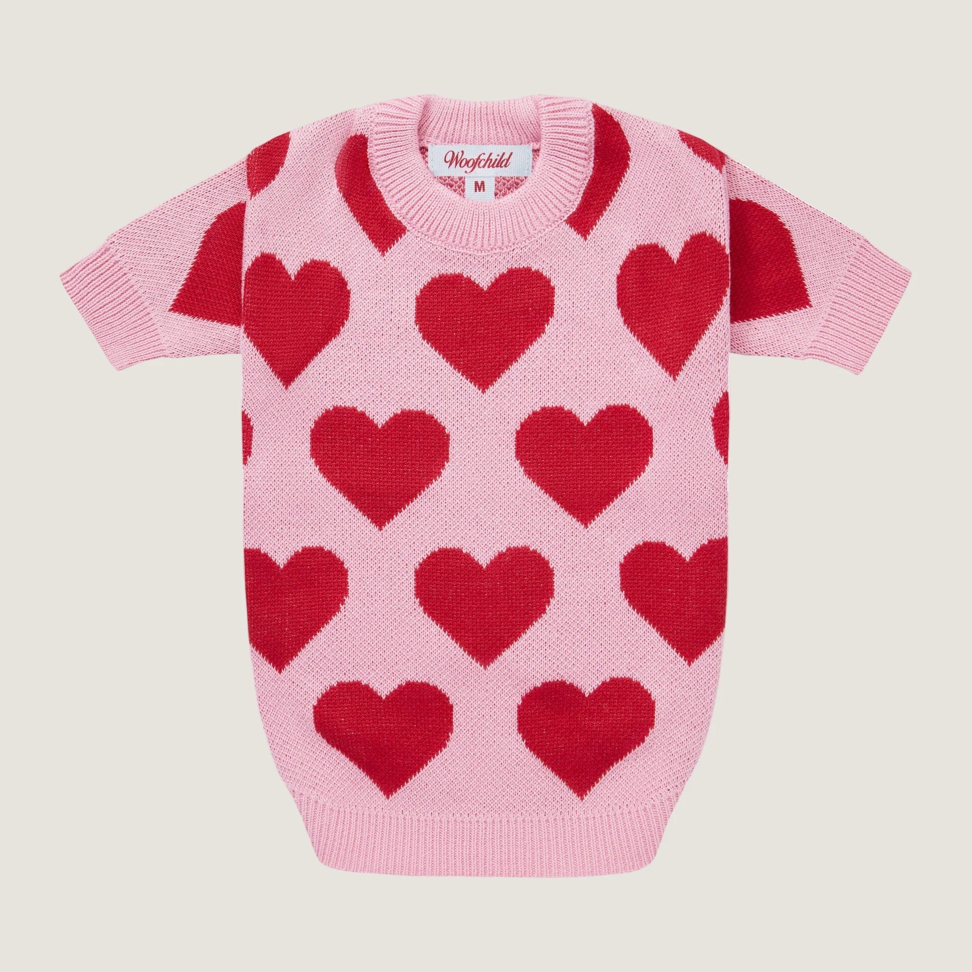 Pink sweater with red heart patterns on a light beige background