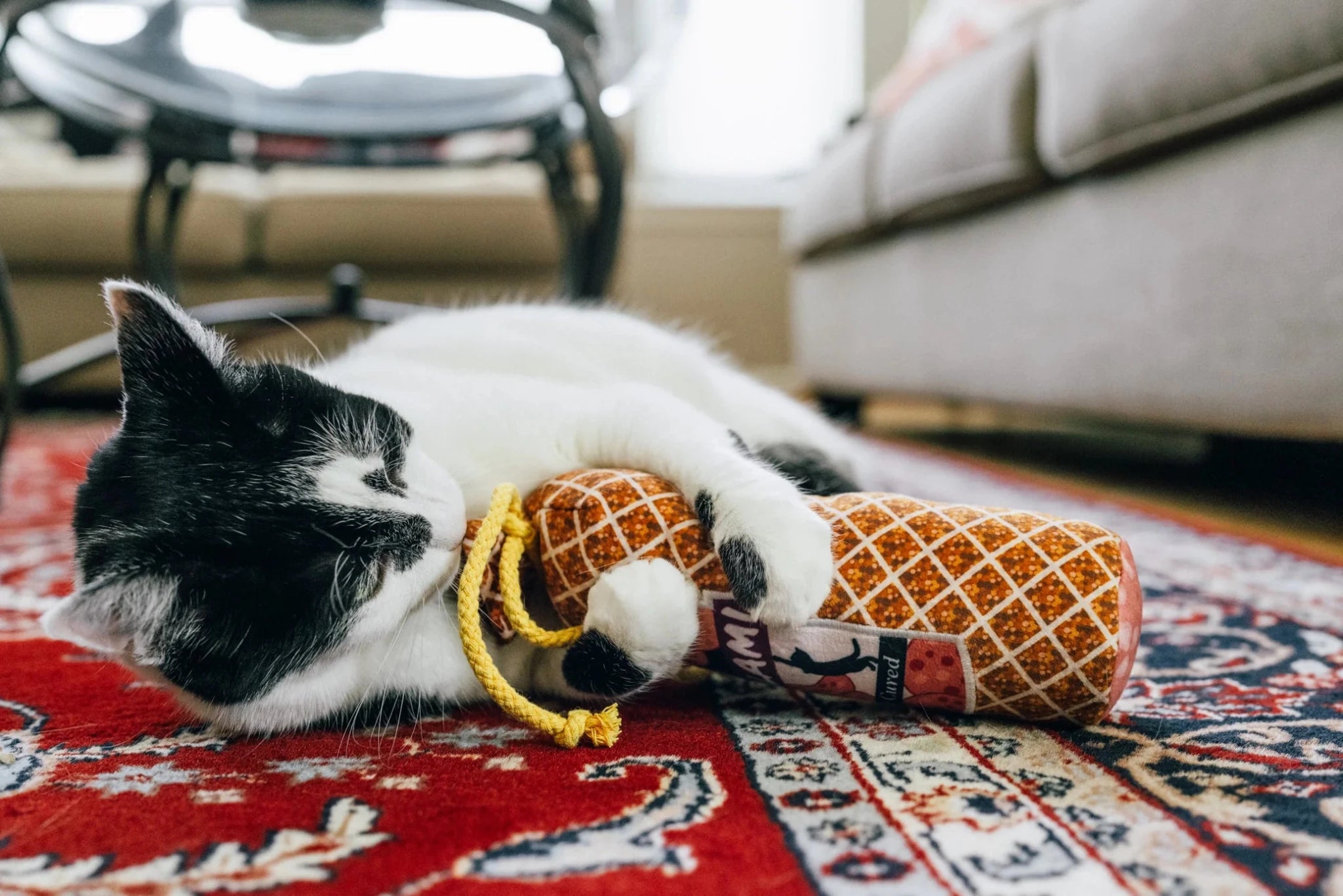 Cat playing with a toy on a patterned rug in a living room.