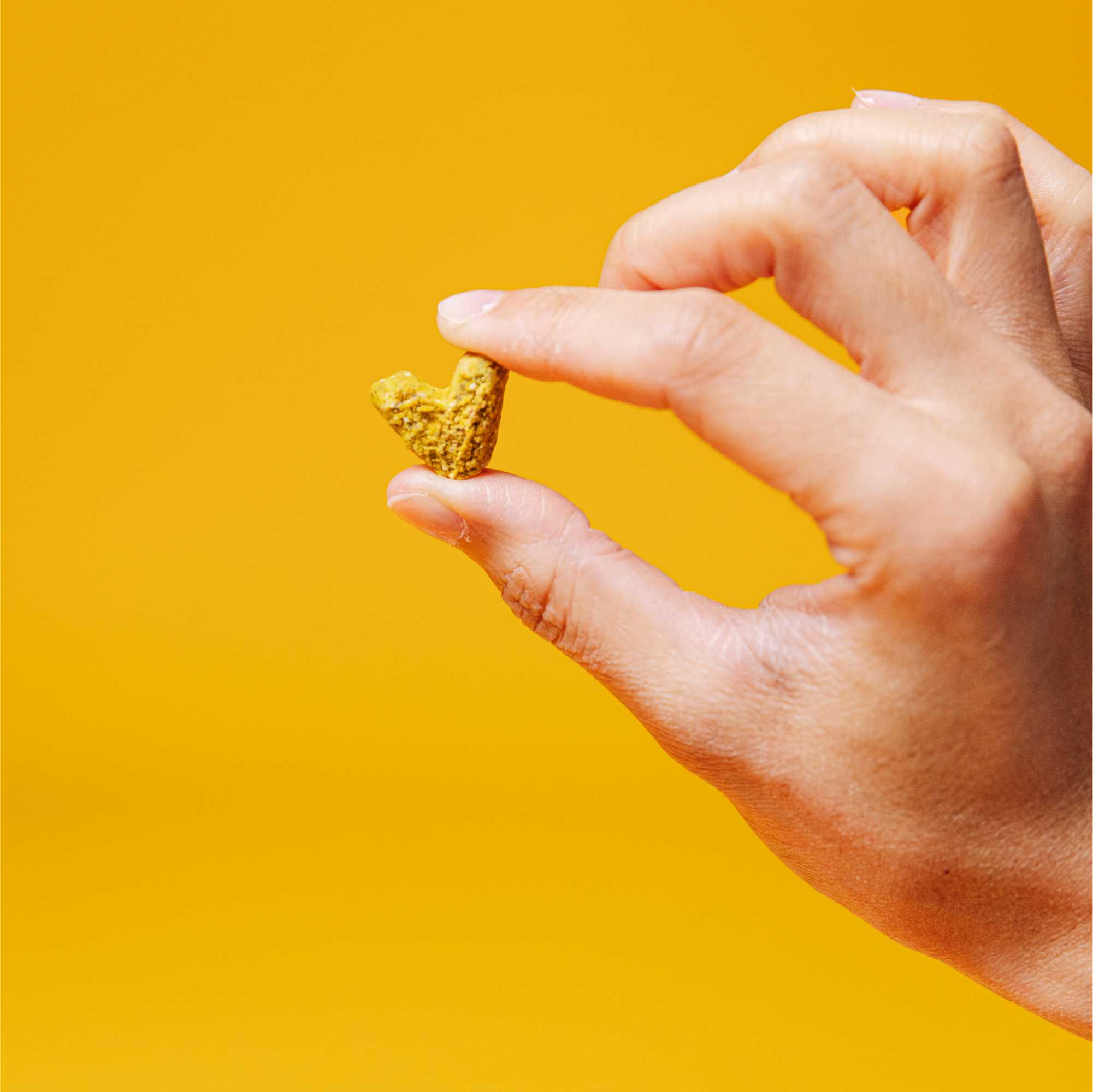 Hand holding a small gold heart-shaped object against a yellow background