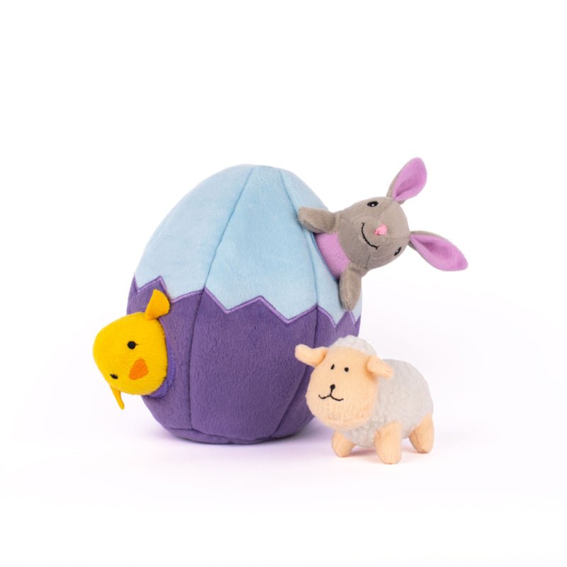 Plush toy rabbit emerging from a purple and blue egg with a duck and sheep toy on a white background