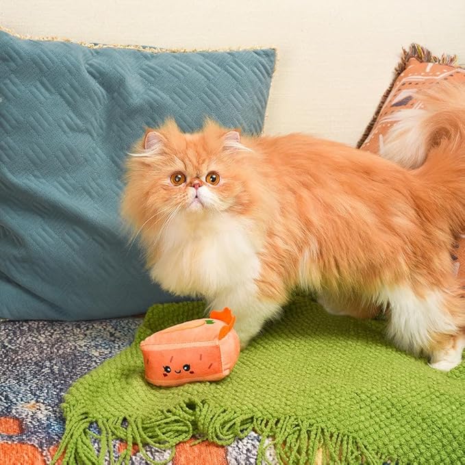 Orange and white cat playing with a small orange toy on a green blanket.