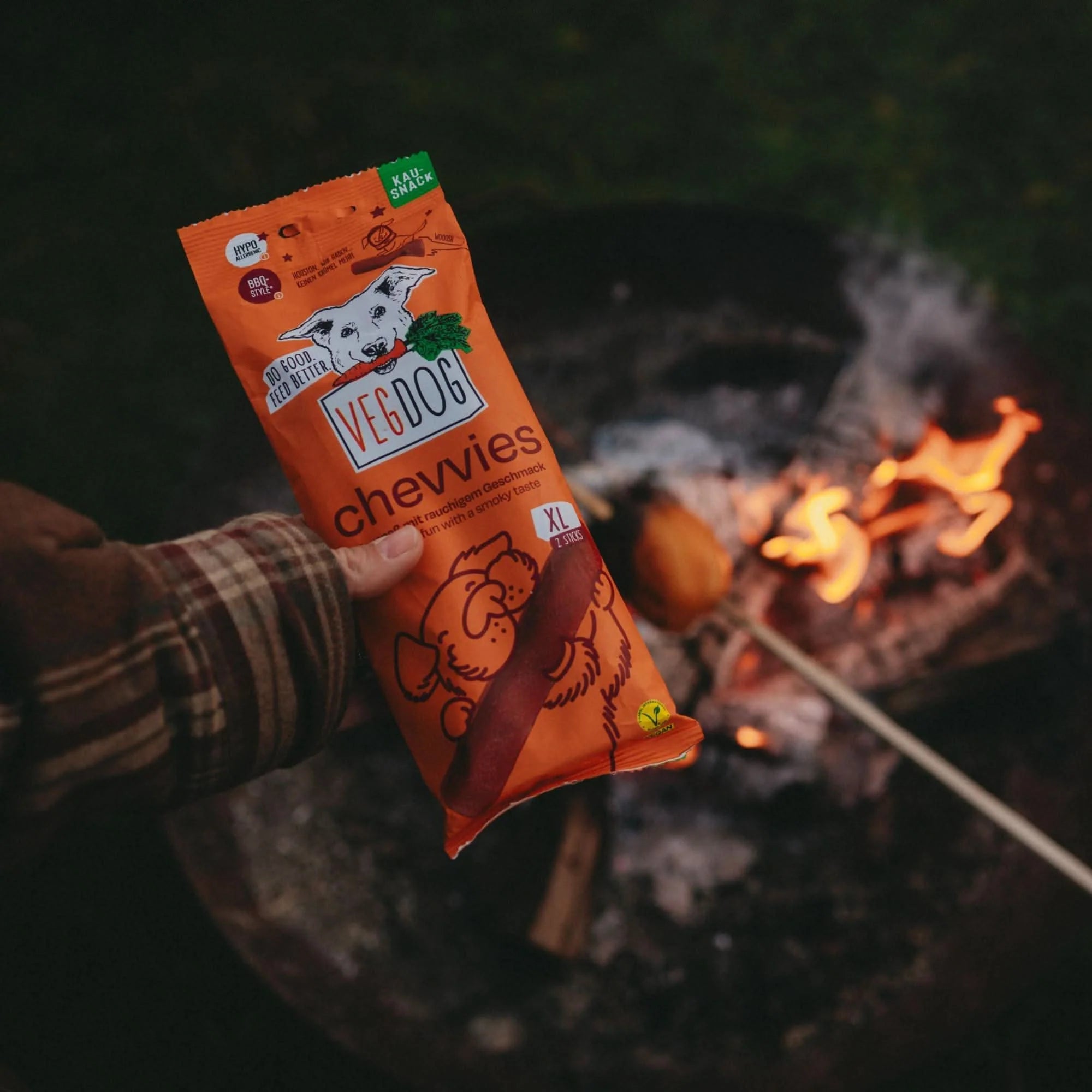 Person holding a package of Veedog Chewies near a campfire
