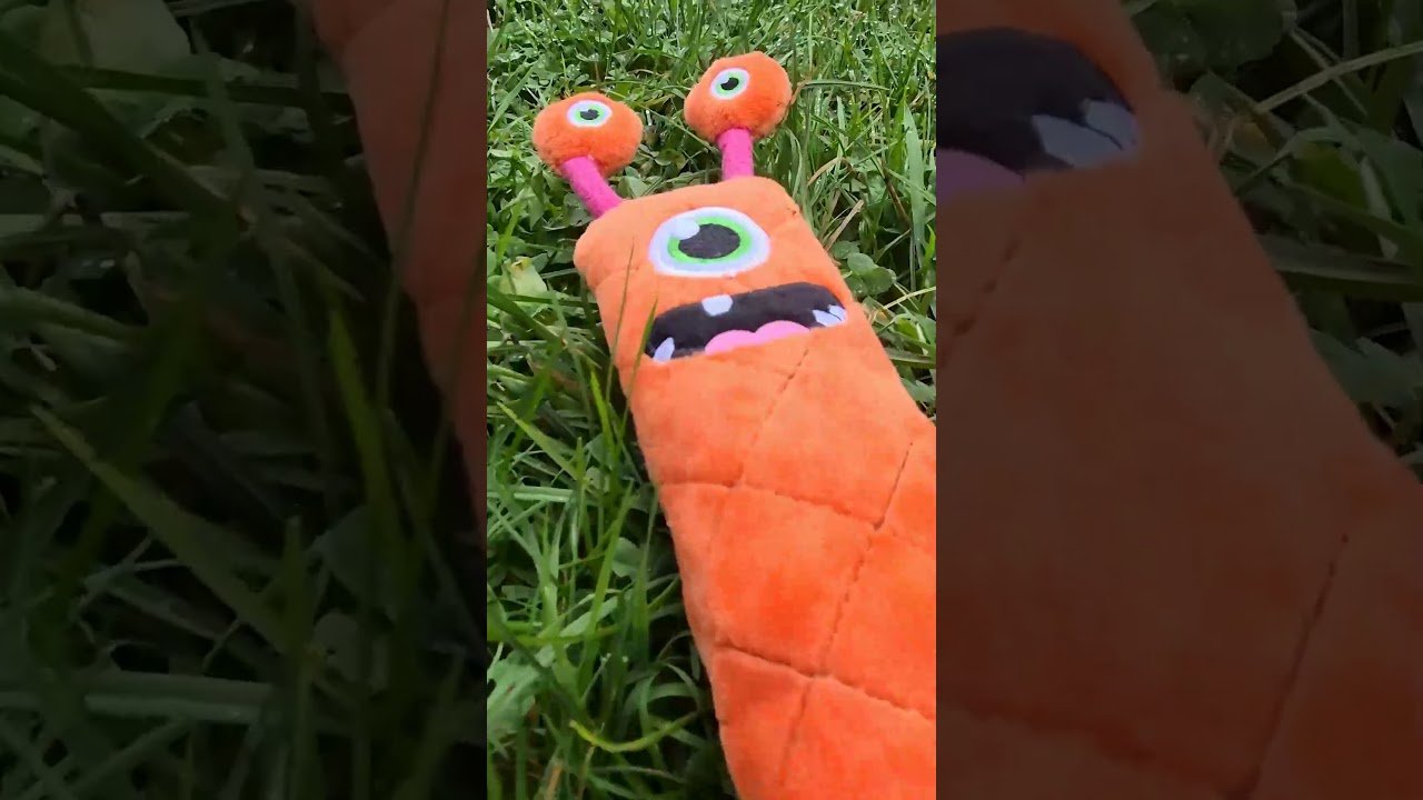 Orange plush toy with a face held in front of grass