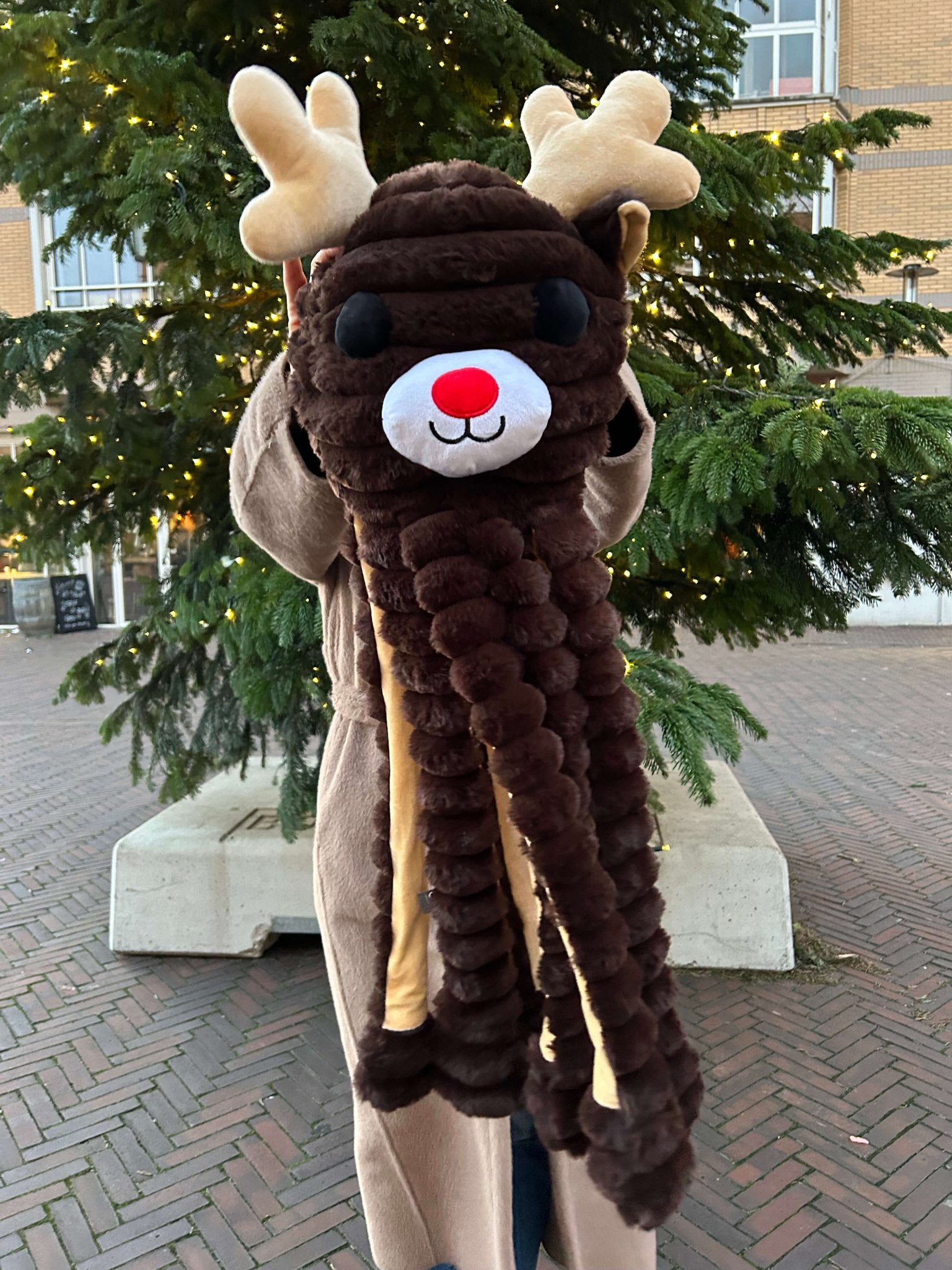 Person wearing a reindeer-themed scarf in front of a Christmas tree.
