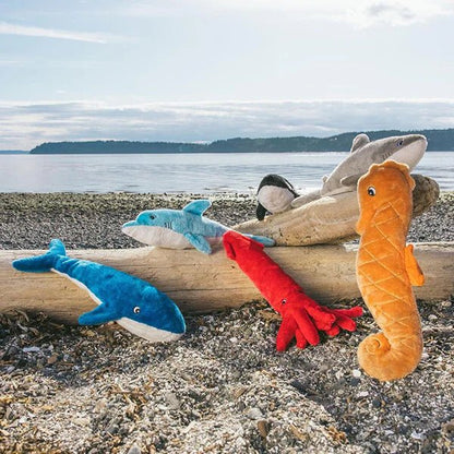 Plush toys resembling a shark, dolphin, and seahorse on a log with a beach background