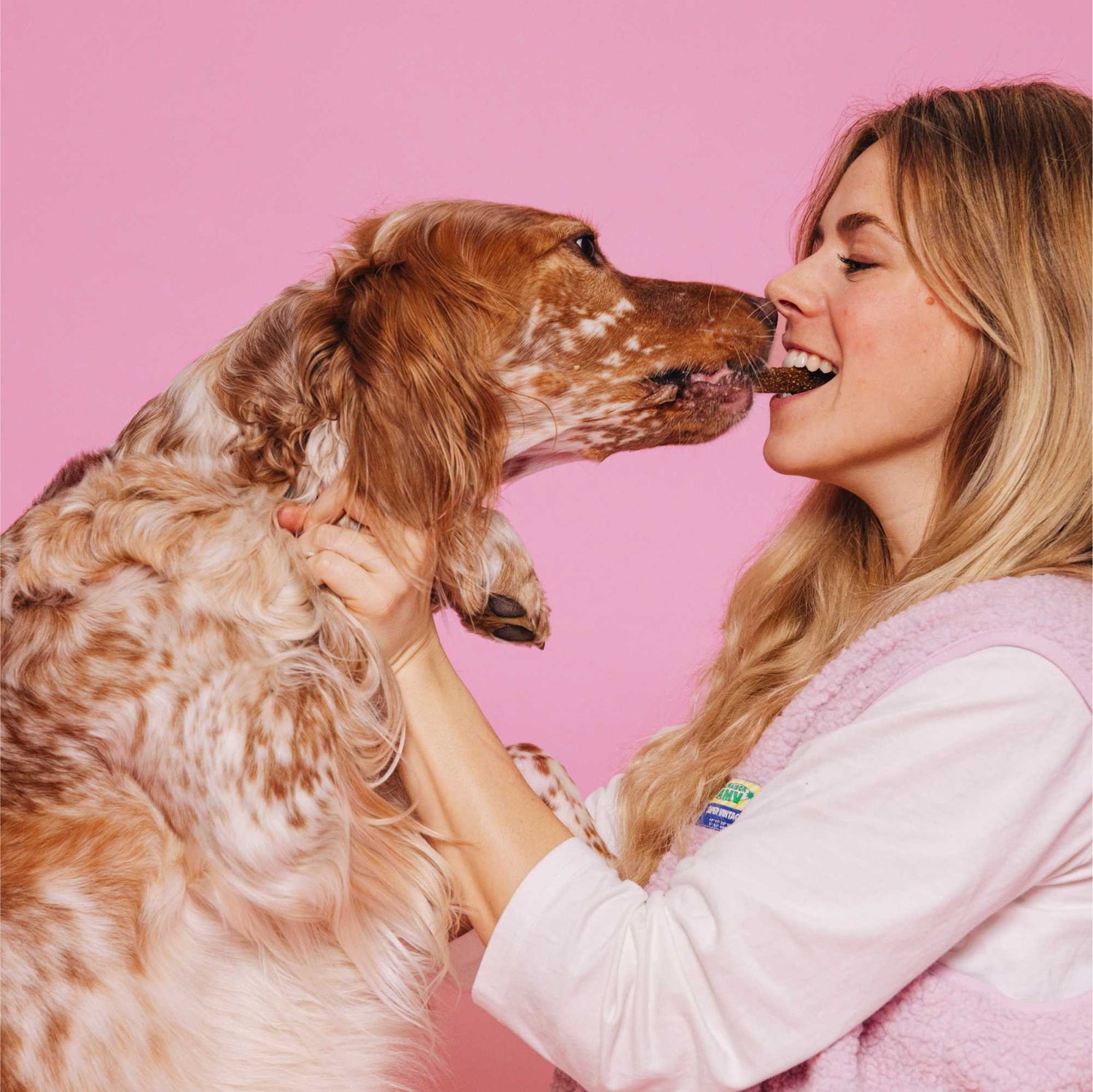 Woman and dog interacting on a pink background