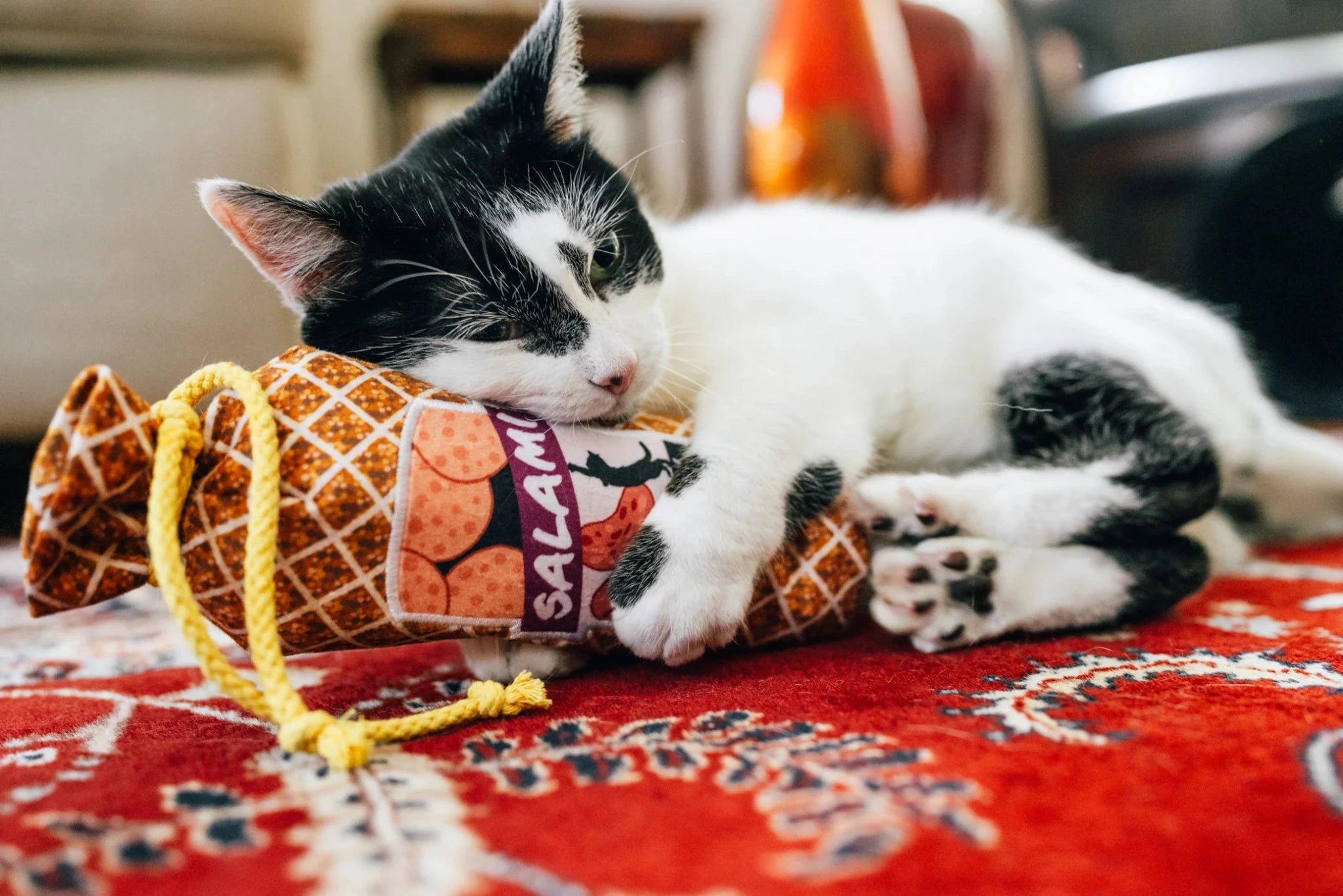 Cat playing with a Halloween-themed bag on a red patterned rug